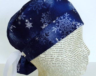 Ponytail Scrub Cap scrub hat featuring a dark blue material with white and silver snowflakes with a winter theme and a white ribbon