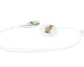 Bracelet with motiv of a leaf from Swedish Lappland and a white satin / macramé ribbon string