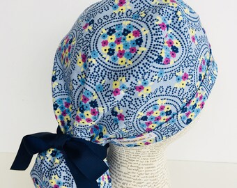 Ponytail Scrub Cap scrub hat featuring a light blue material with flowers in pink yellow and blue with a matching ribbon