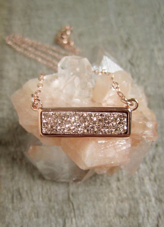A small rose gold and pink crystal bar necklace rests on a small amethyst crystal.