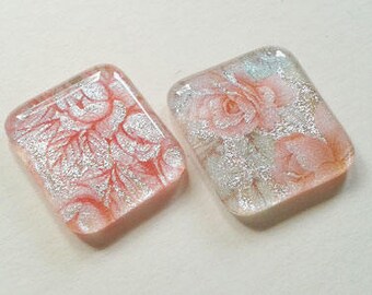 Pair of silver dichroic glass cabochons with pink rose patterns.