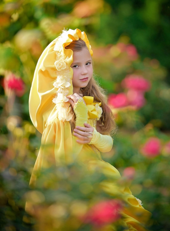 Princess party dresses and more can be found at Ella Dynae Designs. A young girl in a yellow dress and flowered cape stands a field of flowers. 