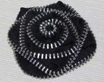 Black zip and metal flower brooch.