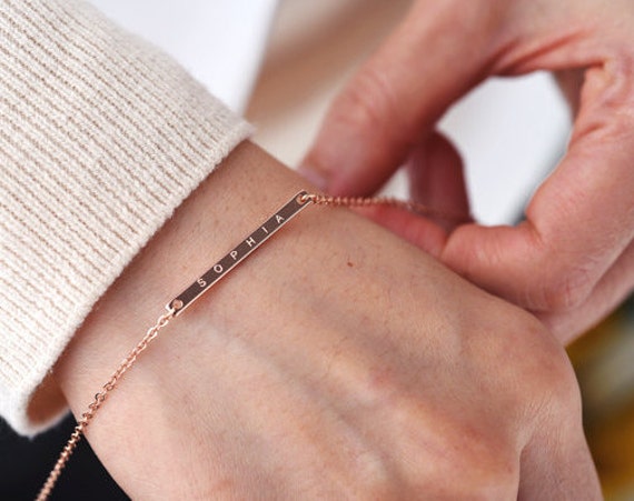 [Image description: A woman's hand displays a minimalistic, rose-gold engraved bracelet that says "Sophia" on it.]