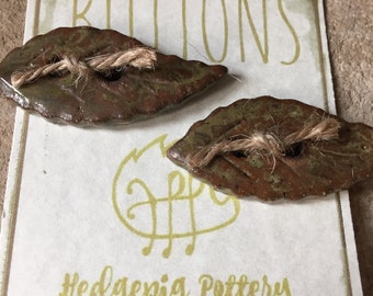 A pair of handmade leaf-shaped olive green ceramic buttons.