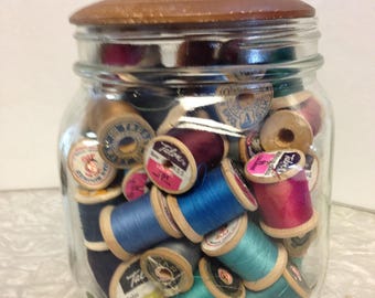 Glass jar with wooden lid full of wooden thread spools