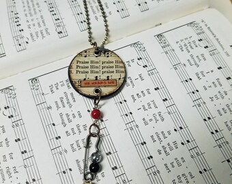 Heartsongs - Praise Him, Praise Him is an altered wood poker chip with paper hymn snippets, metal findings and charms