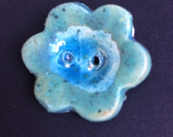 Handmade ceramic flower button in a soft green and blue glaze.