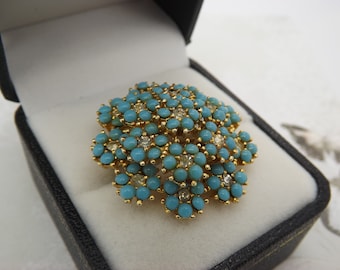 A fine Sphinx round flower head vintage jewelry brooch made in openwork goldtone metal set with turquoise & sparkly clear white glass stones