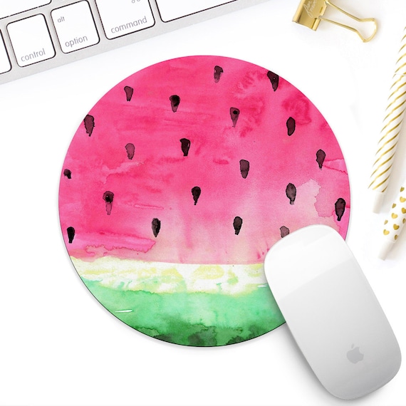 A round mousepad that looks like a watermelon slice, sitting next to a computer keyboard. An apple mouse sits on the mousepad.