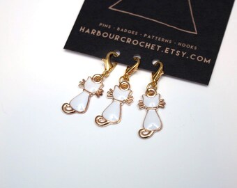 Set of 3 cat shaped stitch markers; gold toned metal with white enamel detail. Choose from lobster clasps or bulb pins