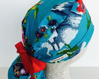 Ponytail Scrub Cap scrub hat featuring a blue material with flowers in shades of blues red green and white with a matching red ribbon