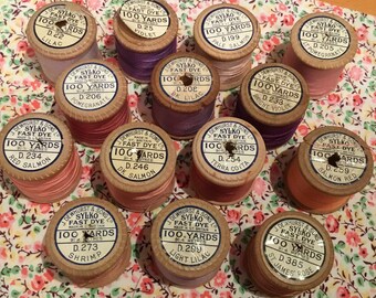 Fourteen Wooden Sylko Reels in various shades of pink purple lilac red