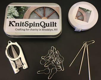 Knitting notions kit - folding scissors, yarn needles, measuring tape, locking stitch markers all nestled in a clamshell metal tin