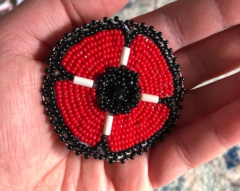 Haudenosaunee made beaded poppy brooch for Remembrance Day/ Veterans featuring white wampum.