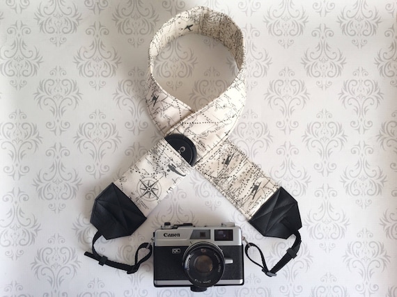 camera with travel themed camera strap on white fleur de lis wallpaper