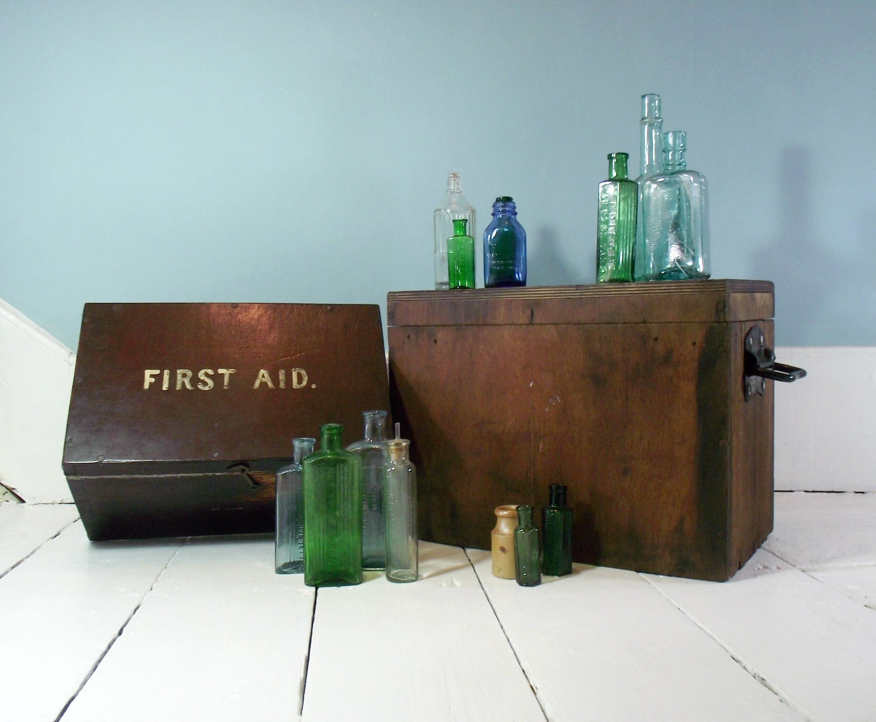 A collection of antique poison bottles and apothecary bottles with a vintage first aid box from the 1920s.